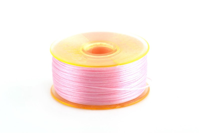 May include: A spool of pink thread wound around a yellow plastic bobbin.