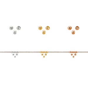 Può includere: Un set di perline dorate, oro rosa e argentate per la creazione di gioielli. Le perline sono piccole e rotonde e sono disposte in fila su uno sfondo bianco.