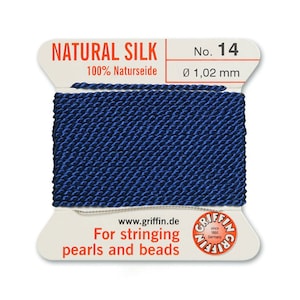 Puede incluir: Una bobina de hilo de seda natural azul oscuro para enhebrar perlas y cuentas. La etiqueta dice "NATURAL SILK 100% Naturseide No. 14 &Oslash; 1,02 mm www.griffin.de For stringing pearls and beads"
