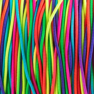 May include: A close-up of a bundle of colorful elastic cords. The cords are arranged in vertical rows and are made of a variety of bright colors, including red, orange, yellow, green, blue, purple, and pink.