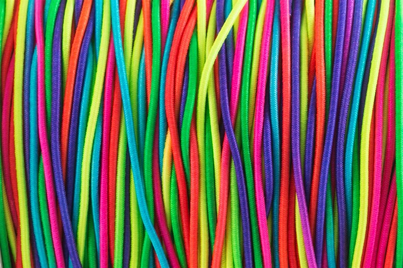 May include: A close-up of a bundle of colorful elastic cords. The cords are arranged in vertical rows and are made of a variety of bright colors, including red, orange, yellow, green, blue, purple, and pink.