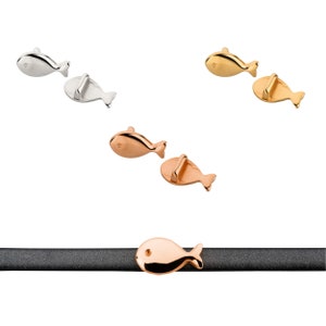 Puede incluir: Tres cierres en forma de pez plateados, dorados y de oro rosa para un brazalete de cuero. Los cierres se muestran en una correa de cuero negra.