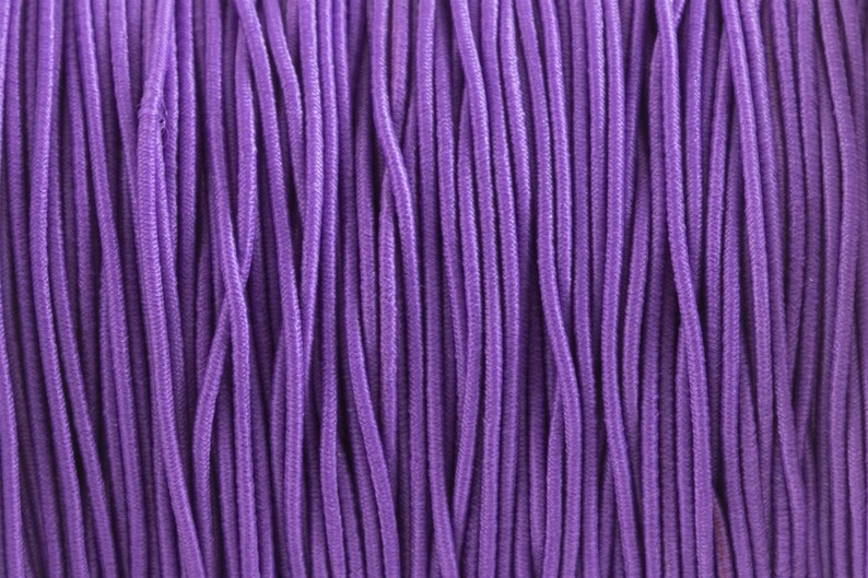 May include: A close-up of a bundle of purple elastic cord. The cord is tightly wound together, creating a textured surface.
