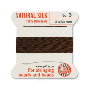 May include: A spool of brown natural silk thread for stringing pearls and beads. The spool is labelled "NATURAL SILK 100% Naturseide No. 3 &Oslash; 0,50 mm" and "For stringing pearls and beads".