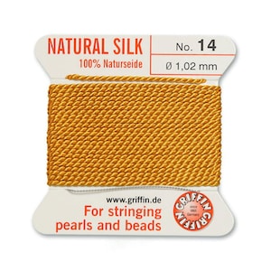 Puede incluir: Una bobina de hilo de seda natural de color dorado para enhebrar perlas y cuentas. La etiqueta dice "NATURAL SILK 100% Naturseide No. 14 &Oslash; 1,02 mm www.griffin.de For stringing pearls and beads GRIFFIN"