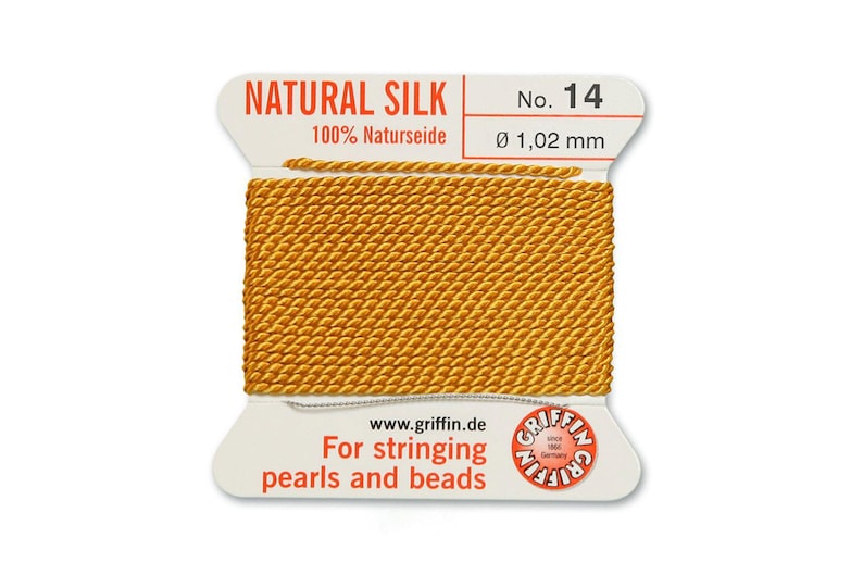 Puede incluir: Una bobina de hilo de seda natural de color dorado para enhebrar perlas y cuentas. La etiqueta dice "NATURAL SILK 100% Naturseide No. 14 &Oslash; 1,02 mm www.griffin.de For stringing pearls and beads GRIFFIN"