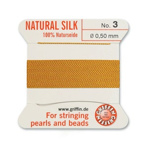 May include: A spool of gold-coloured natural silk thread for stringing pearls and beads. The label reads "NATURAL SILK 100% Naturseide No. 3 &Oslash; 0,50 mm www.griffin.de For stringing pearls and beads"