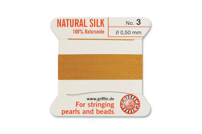 May include: A spool of gold-coloured natural silk thread for stringing pearls and beads. The label reads "NATURAL SILK 100% Naturseide No. 3 &Oslash; 0,50 mm www.griffin.de For stringing pearls and beads"