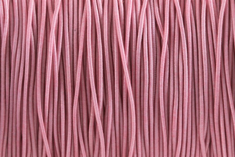 May include: Close-up of a spool of pink elastic cord. The cord is tightly wound and has a smooth, shiny finish.