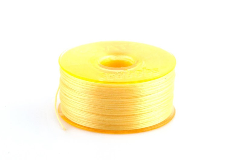 May include: A spool of yellow thread with a clear plastic bobbin.