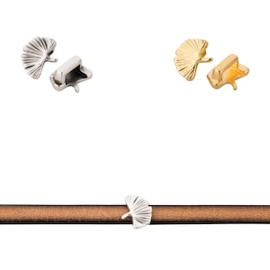 Könnte beinhalten: Zwei silberne und zwei goldene Ginkgoblatt-Charm-Verschlüsse für Lederarmbänder. Die Verschlüsse sind auf einem braunen Lederband gezeigt.