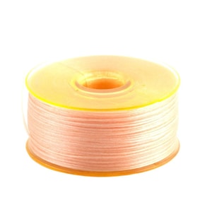 May include: A spool of pale pink thread wound around a yellow plastic bobbin.