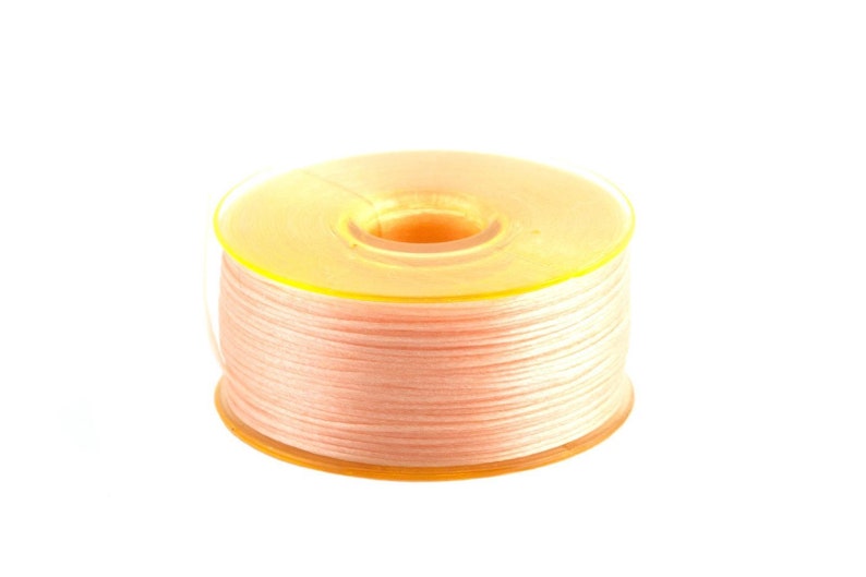 May include: A spool of pale pink thread wound around a yellow plastic bobbin.