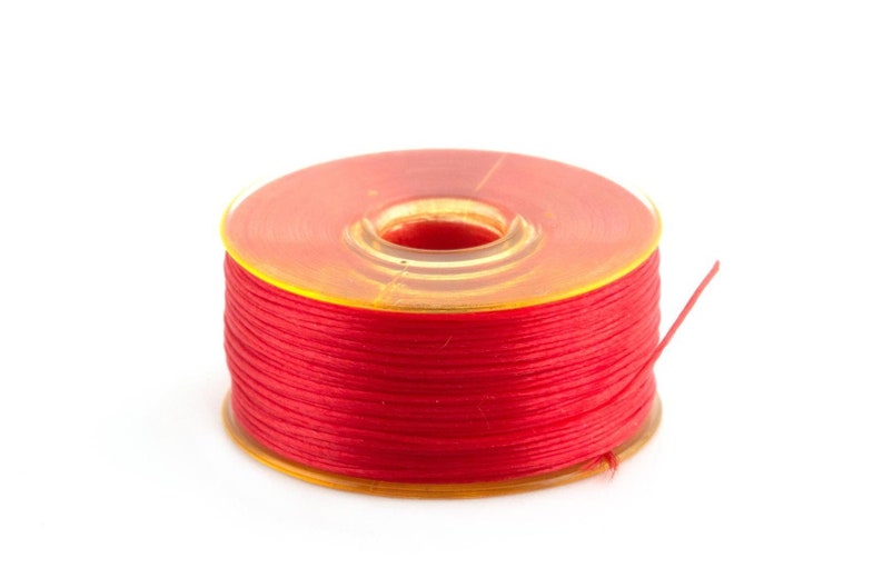 May include: A spool of red thread wound around a clear plastic bobbin.