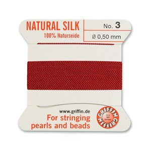 May include: A spool of red natural silk thread for stringing pearls and beads. The spool is labelled "NATURAL SILK 100% Naturseide No. 3 &Oslash; 0,50 mm" and "For stringing pearls and beads".