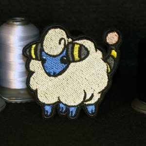 May include: An embroidered patch of a sheep-like Pokemon with blue and yellow accents. The Pokemon is white and fluffy, with a black tail and a pink nose.