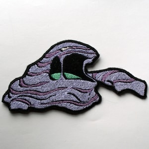 May include: Purple and black embroidered patch shaped like a cartoon monster with a green eye.