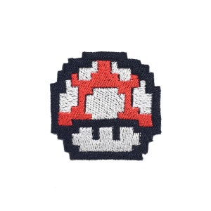 Puede incluir: Un parche bordado de un hongo pixelado rojo y blanco. El hongo está rodeado de negro.