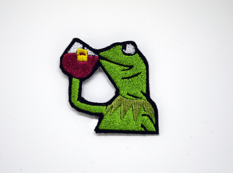 May include: Green embroidered iron-on patch of a frog drinking from a red cup with a yellow lid. The frog has a surprised expression with its eyes wide open.