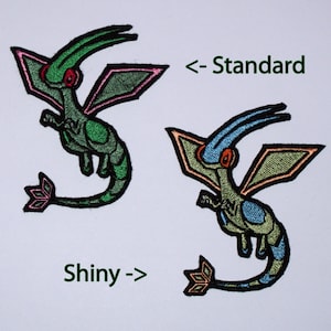 Puede incluir: Dos parches bordados de un personaje Pokemon verde y azul con el texto "< - Standard" y "Shiny ->".