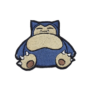 May include: Embroidered patch depicting a blue and tan cartoon character. The character has a round body, small limbs, and a sleepy expression. The patch is designed for application on clothing or accessories.