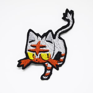 Op de afbeelding: Geborduurde strijkpatch met een cartoonkat met rode, witte en zwarte strepen. De kat heeft gele ogen en een rode ster op zijn voorhoofd.