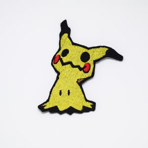 May include: Yellow embroidered iron-on patch of a cartoon ghost-like Pokemon character with black outlines and red cheeks.