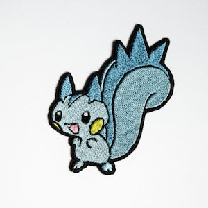 May include: An embroidered iron-on patch featuring a blue and yellow cartoon squirrel with a spiky tail. The squirrel is smiling and has a yellow ear.