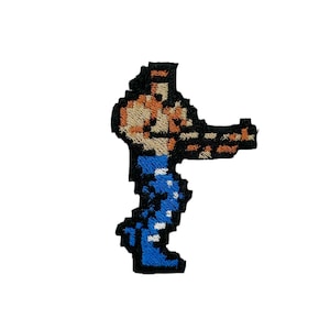 May include: Embroidered patch of a pixelated video game character. The character is wearing blue pants and a brown shirt. The character is facing right and has a determined expression.
