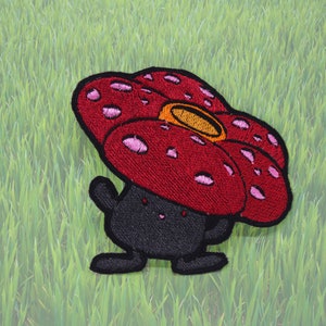 May include: A red and pink embroidered patch of a cartoon character with a large flower-shaped head and a black body. The character has a small mouth and two small eyes.