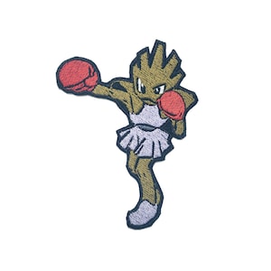 May include: An embroidered patch of a brown and tan Pokemon character wearing boxing gloves. The character is in a fighting pose with one arm raised and the other arm extended forward. The character is wearing a purple and white skirt.