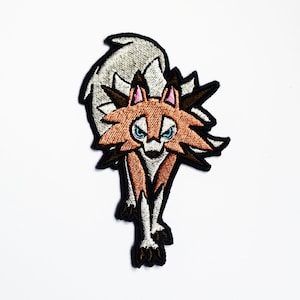 May include: Embroidered patch of a brown and white wolf with blue eyes. The wolf is standing on all fours and has a fierce expression.