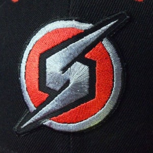 May include: A black baseball cap with a red and silver embroidered logo. The logo is a stylised letter "S" with a lightning bolt through it.