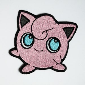 Puede incluir: Parche bordado con un personaje de dibujos animados rosa con grandes ojos azules, orejas negras y un mechón de pelo rizado. El parche tiene un borde negro, para ropa o accesorios.