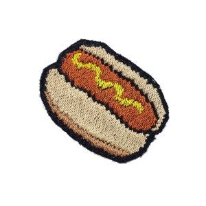 May include: A brown and yellow embroidered hot dog in a white bun.