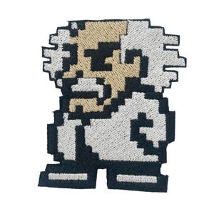 May include: Embroidered patch featuring a pixelated image of a character with white hair and a white lab coat. The character has a tan face and black details. The patch is outlined in black and has a retro video game aesthetic.