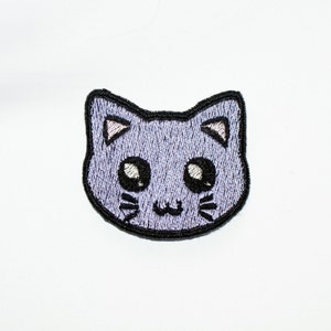 May include: An iron-on patch featuring a cartoon cat with large eyes and whiskers, embroidered in purple.