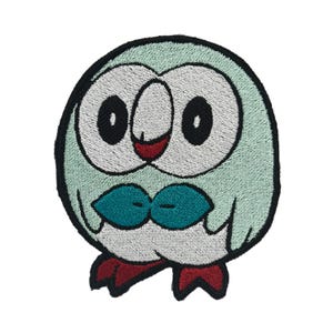 May include: Embroidered patch of a green and white owl-like Pokemon character with red feet and blue wings. The character has large, black eyes and a red mouth.