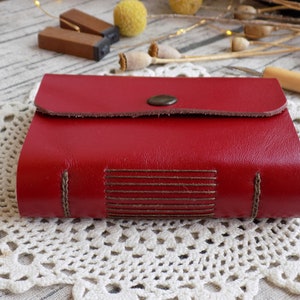 May include: A red leather-bound journal with a flap closure and a decorative button. The journal has brown stitching and a textured leather cover.