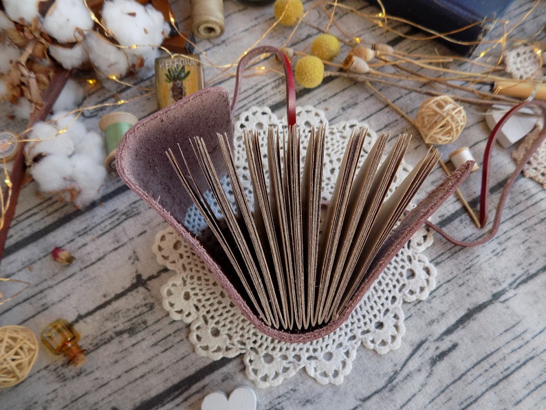 May include: A brown leather-bound journal with a burgundy cover and a lace doily underneath. The journal is open, revealing blank pages.