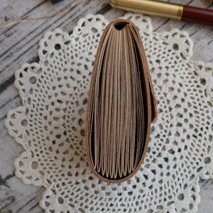 May include: A brown leather-bound journal with a spine that is closed and visible. The journal is lying on a white crocheted doily.
