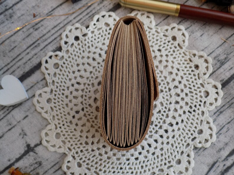 May include: A brown leather-bound journal with a spine that is closed and visible. The journal is lying on a white crocheted doily.
