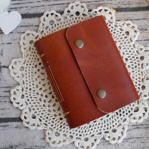 May include: A brown leather journal with a flap closure and two metal clasps. The journal is sitting on a white crocheted doily.