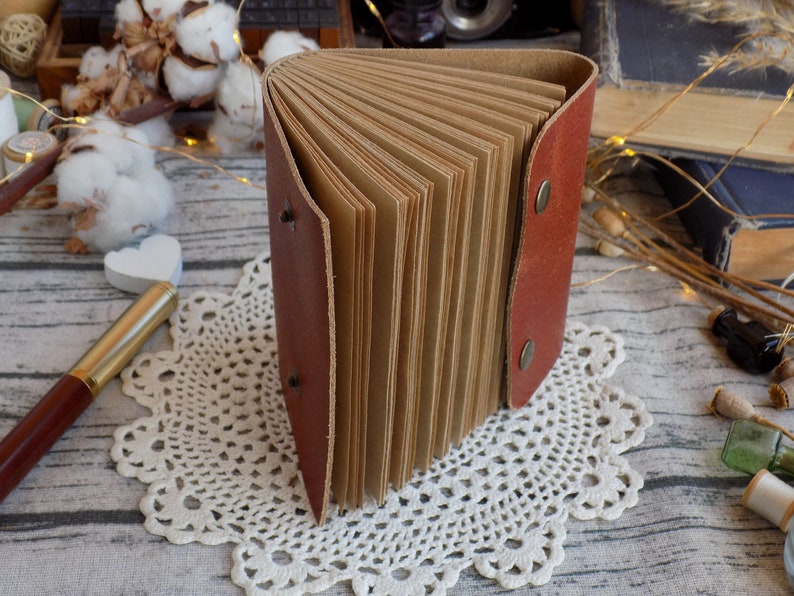 May include: A brown leather-bound journal with blank pages, open to reveal the pages. The journal is sitting on a white doily.