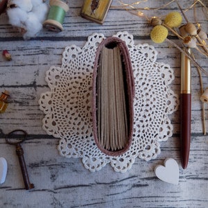 May include: A pink leather-bound journal with a white lace doily and a gold pen on a wooden surface.