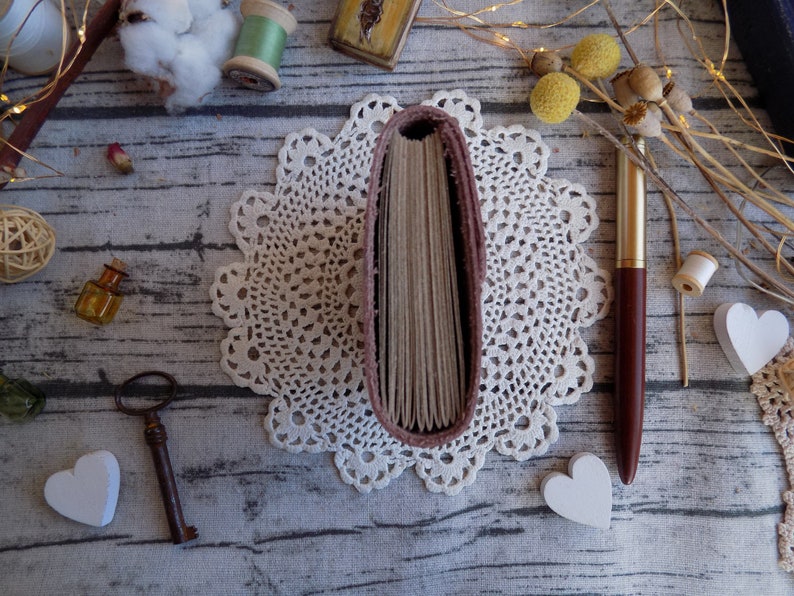 May include: A pink leather-bound journal with a white lace doily and a gold pen on a wooden surface.