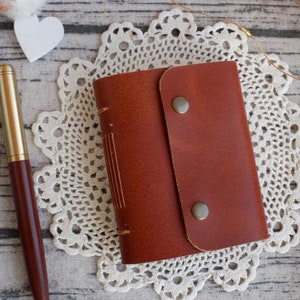 May include: A brown leather-bound journal with a flap closure and two brass clasps. The journal is sitting on a white doily.