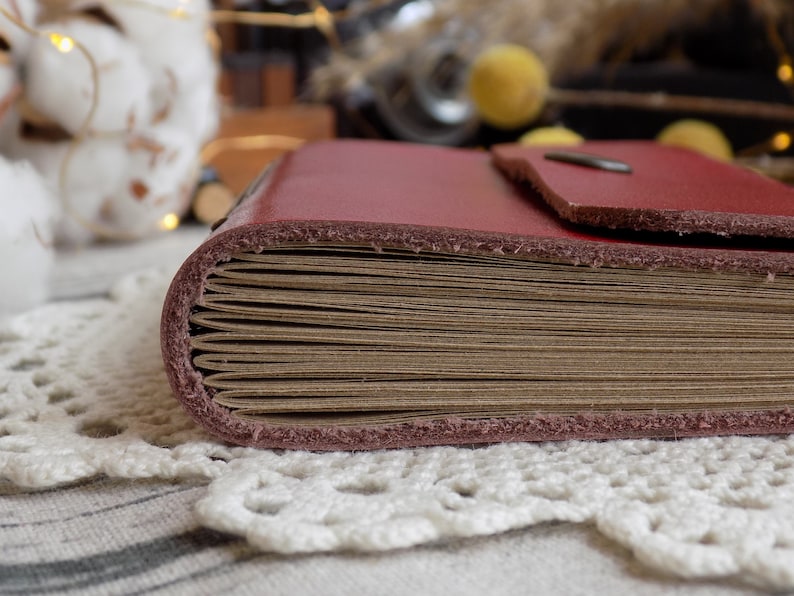 May include: A burgundy leather-bound journal with a thick stack of blank pages. The journal is closed and lying on a white crocheted doily.