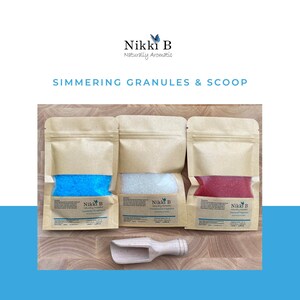 May include: Three brown paper pouches filled with colourful bath salts. The pouches are labelled "Nikki B Naturally Aromatic" and have different scents: Lavender, Eucalyptus, and Rosemary. A wooden scoop is included.