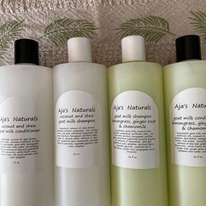May include: Four bottles of Aja's Naturals goat milk shampoo and conditioner. The bottles are white with black or white caps and labels. The labels list ingredients and product names, including coconut and shea, lemongrass, ginger root, and chamomile. Each bottle is 16 fl oz.